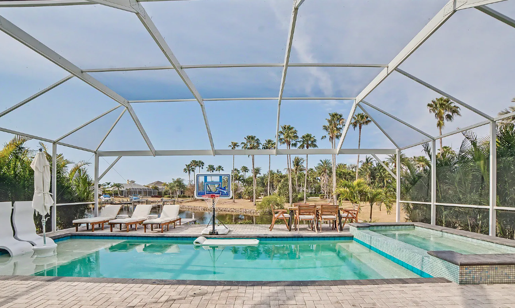 A screened saltwater pool and spa overlooking a palm-lined canal